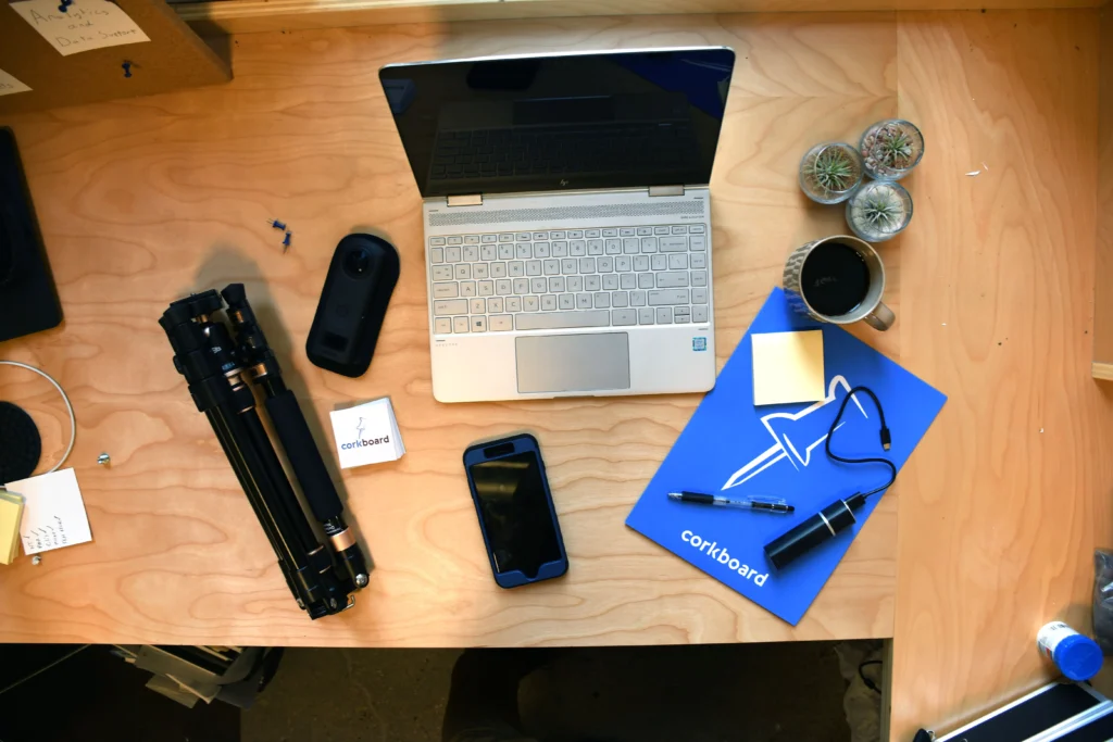 lap top, tri-pod, phone, and other desk items laid out on a wood desk