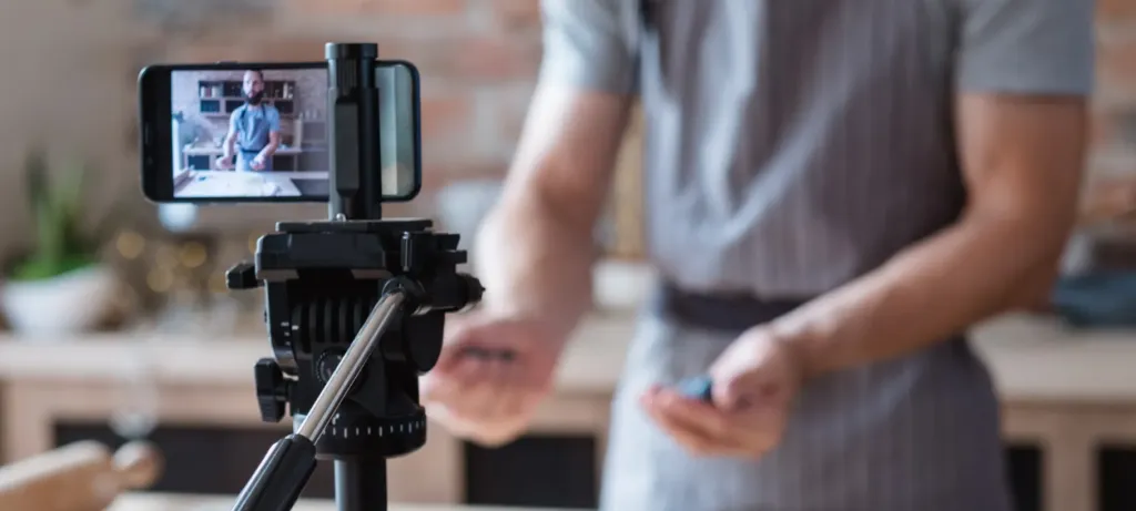 Man in background recording video with phone and tripod in foreground